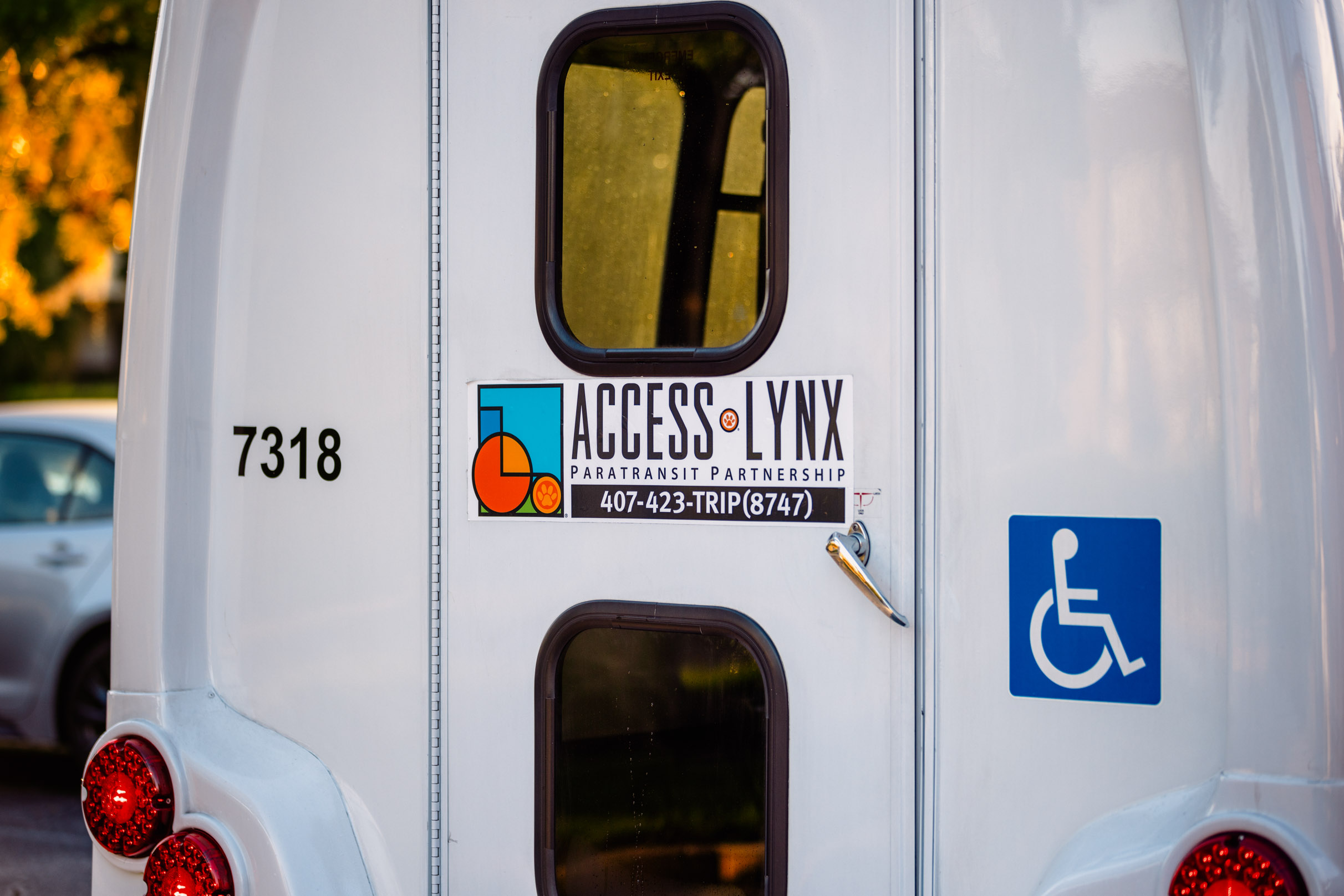 Rear view of a white paratransit vehicle with ACCESS LYNX logo and a wheelchair accessibility symbol on the back door.